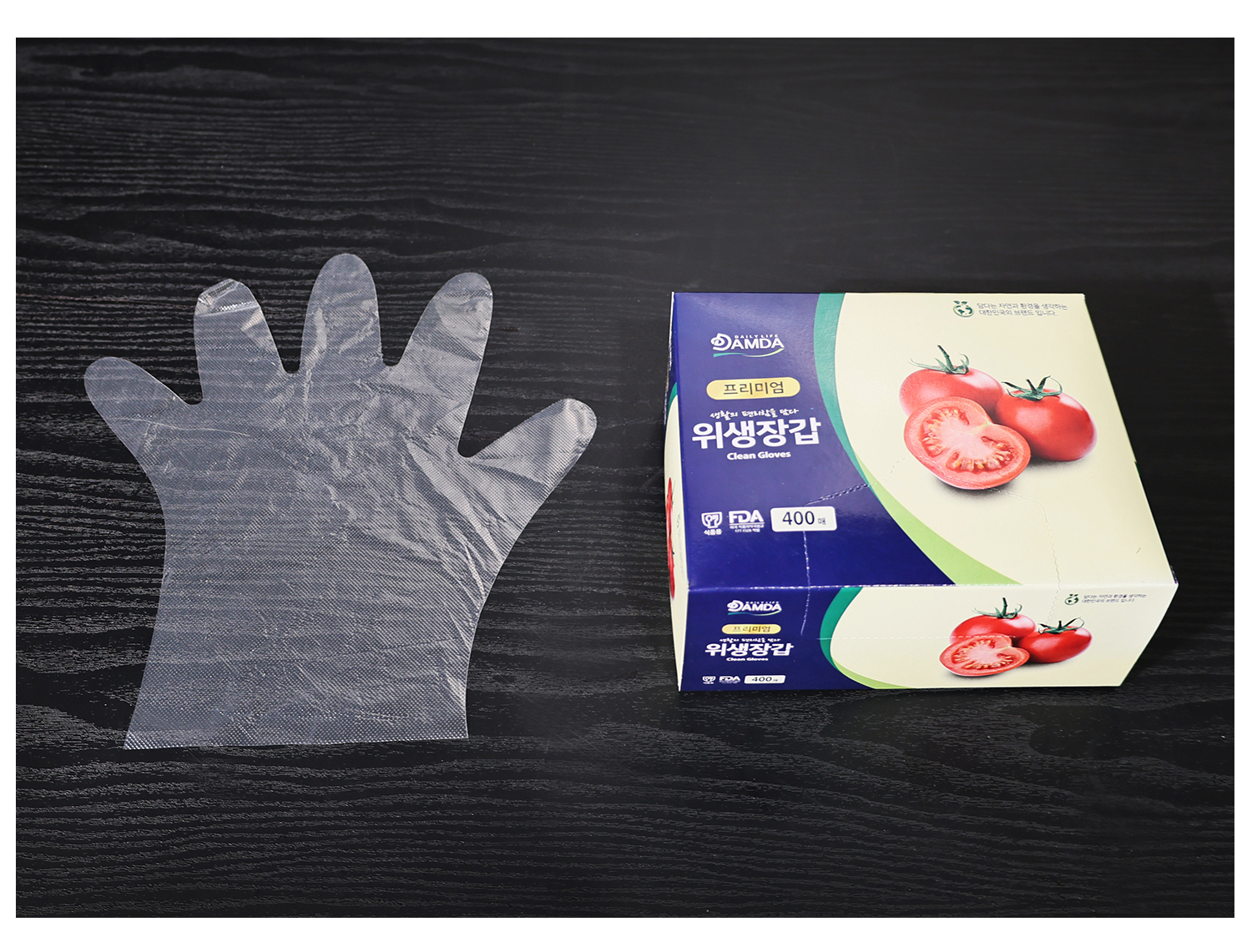 투명한 위생장갑 한 장이 검은 테이블 위에 펼쳐져 비닐장갑의 전체 크기와 손가락 형태가 잘 드러남