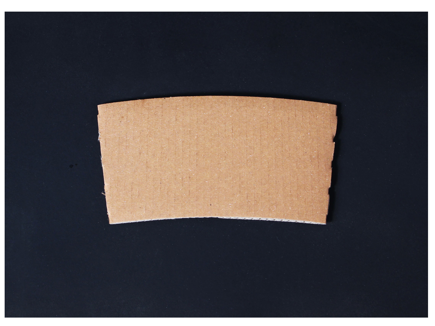 어두운 바닥 배경에 크라프트 재질의 무인쇄 컵홀더가 놓여있다.