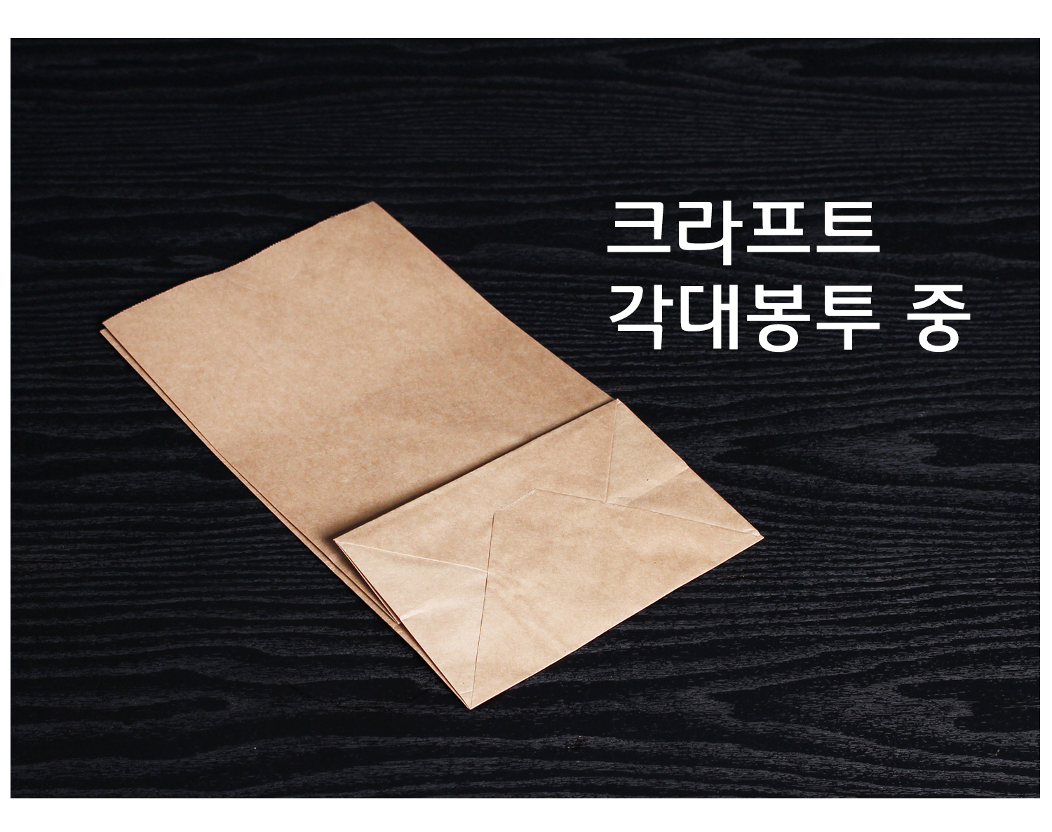 검정 배경에 얇게 접힌 상태의 크라프트 종이 각대봉투 하나가 놓여 있으며, 사용 전의 평평한 형태를 보여주는 구성.